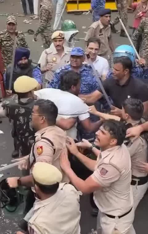 Uniformed personnel moving a man in a white shirt